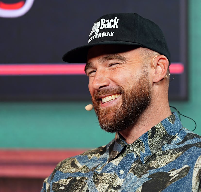 Man with beard laughing, wearing a camo shirt and black cap that says "JumpBack Yesterday." He is ou...
