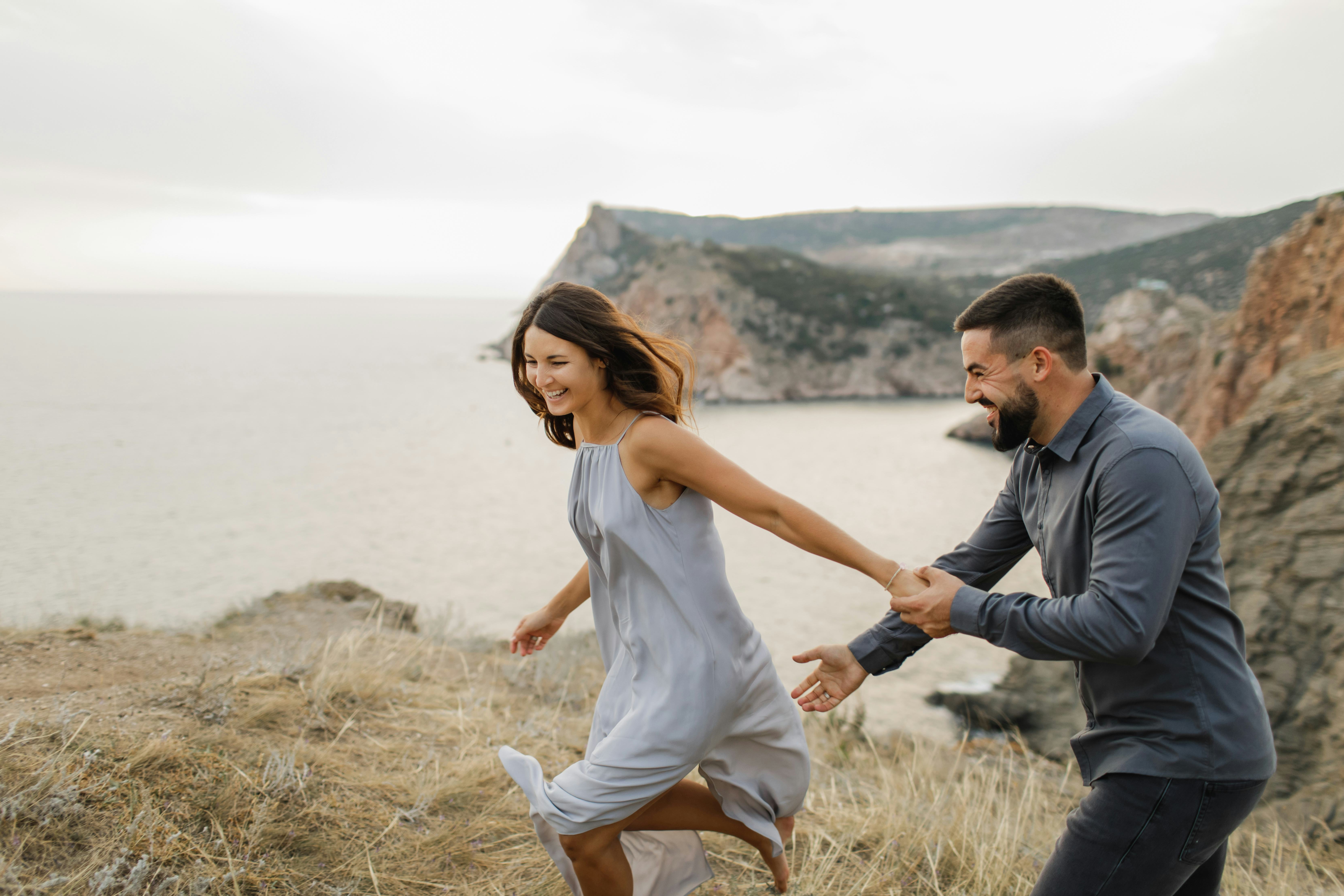 A girlfriend and boyfriend giving each other goofy nicknames as they run and laugh on a cliffside.