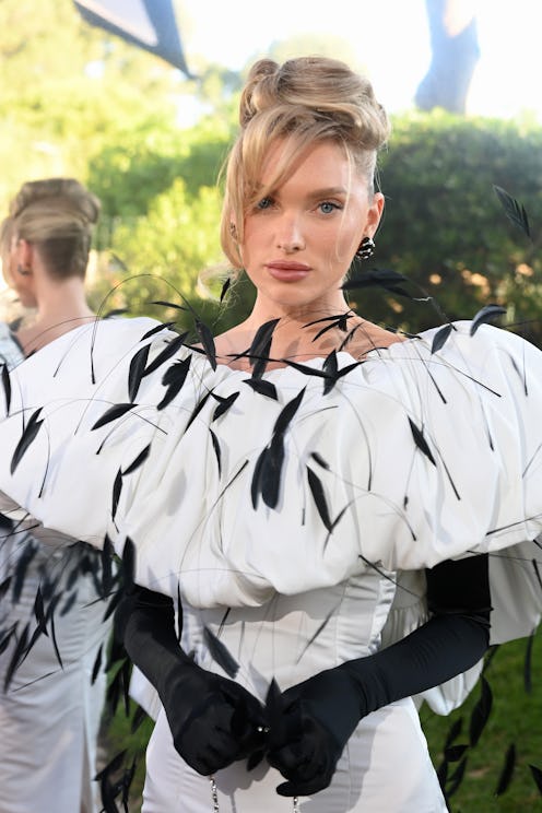 Woman in a white feathered dress with black accents, wearing long black gloves, looking at the camer...