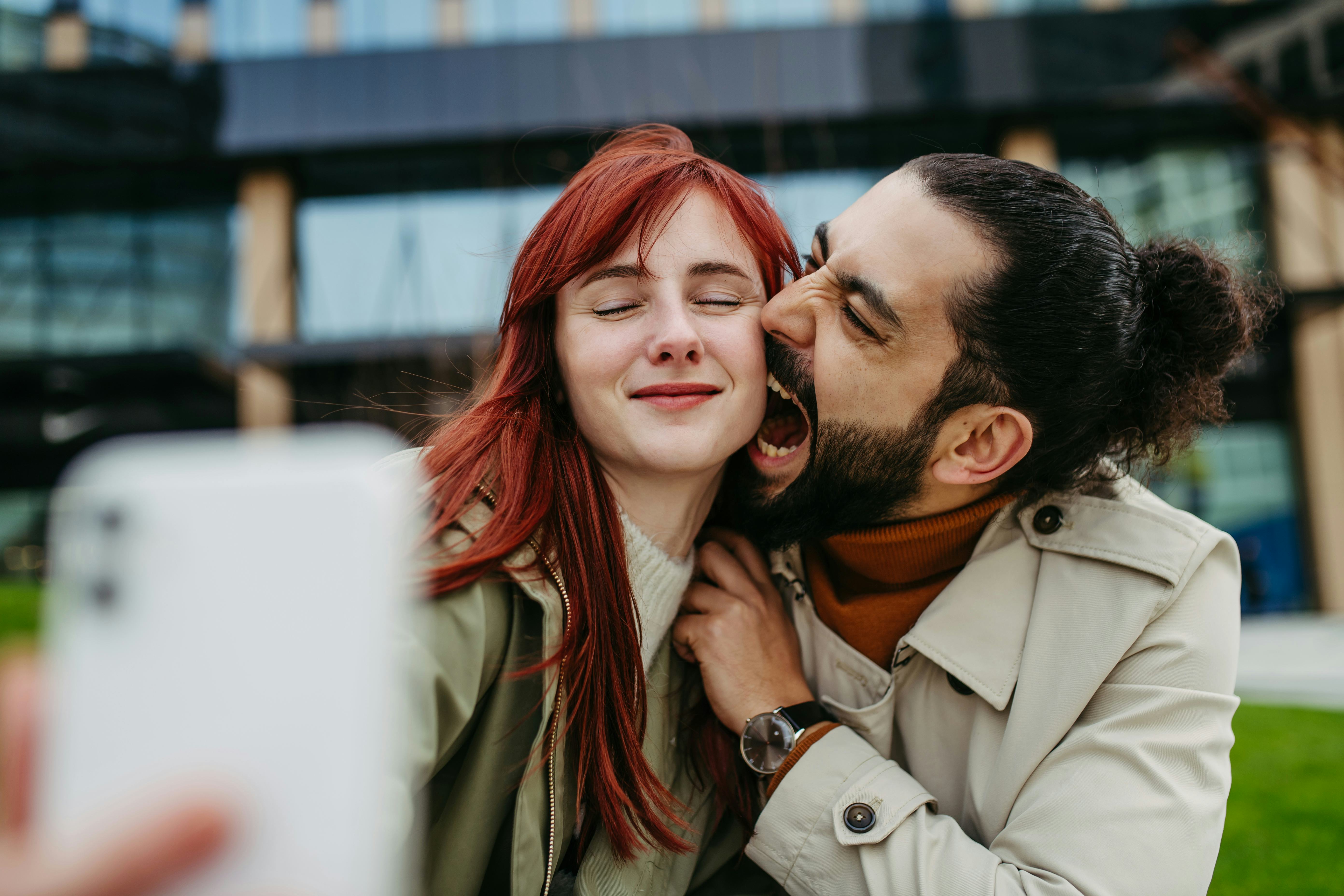 A man bites his girlfriend&rsquo;s cheek as she takes a selfie because she gave him a funny boyfriend nick&hellip;