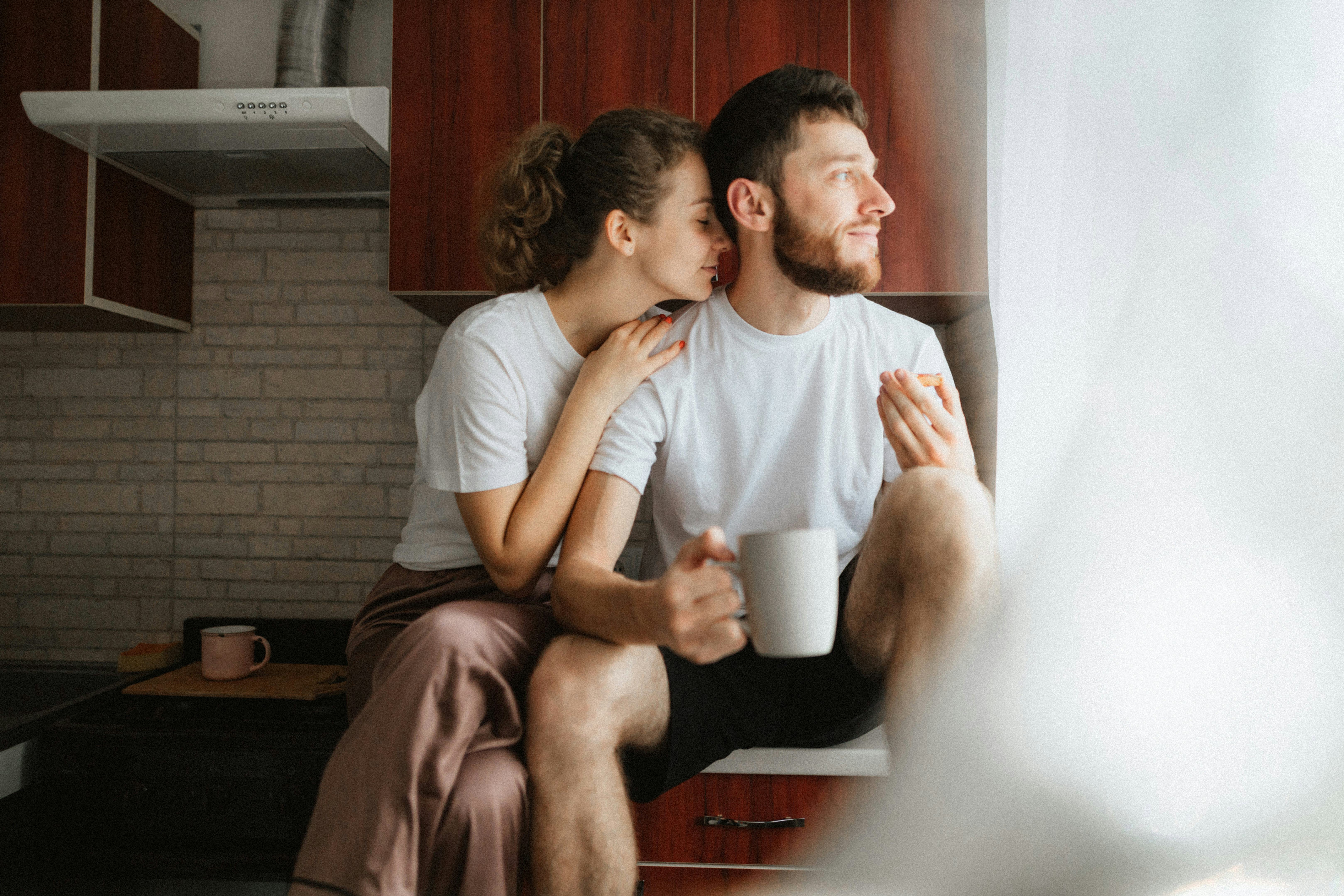 A sweet couple sits on their kitchen counter with coffee giving each other cute nicknames.