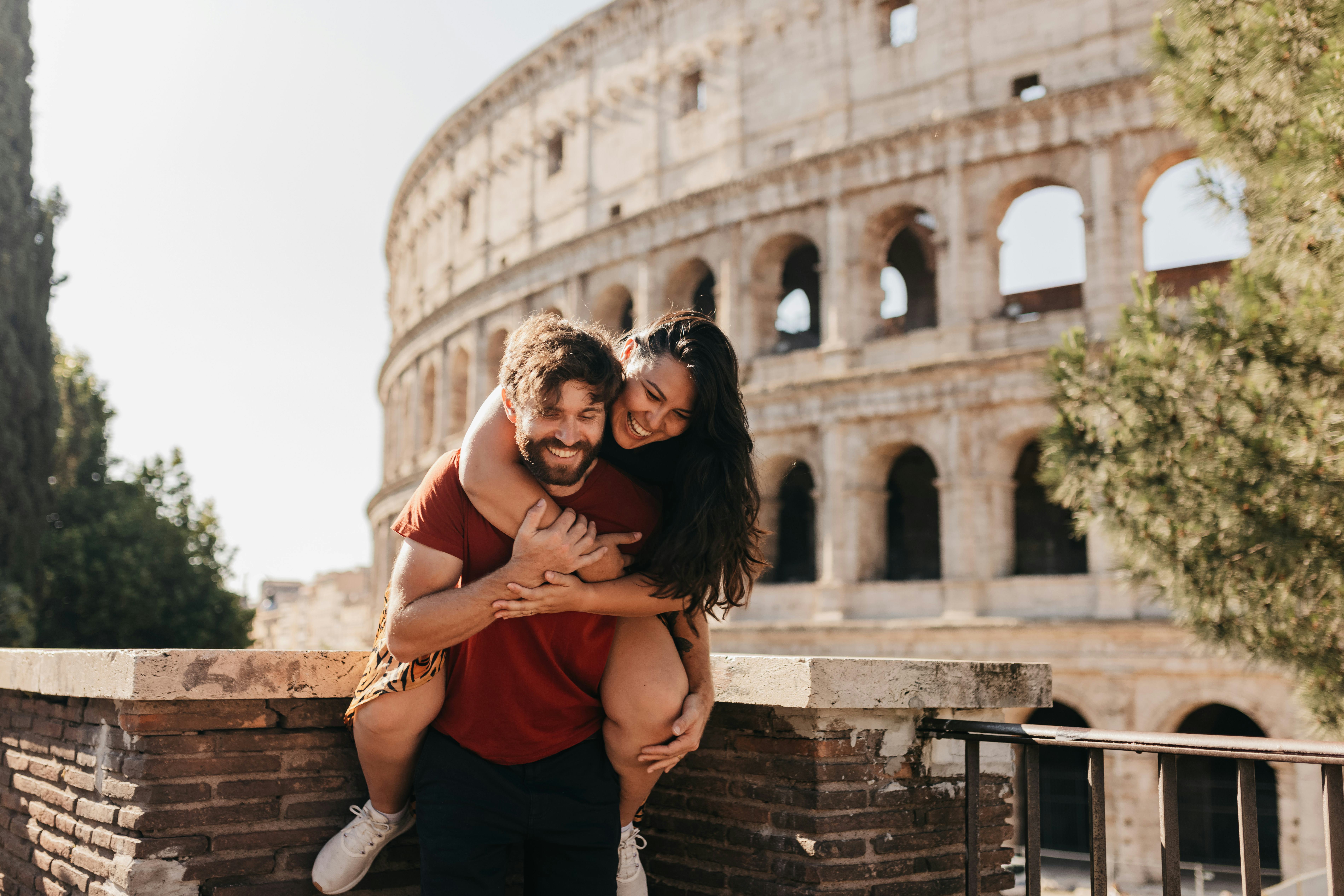 A woman on her boyfriend&rsquo;s back giving him fun nicknames in front of the Colosseum in Rome, Italy.