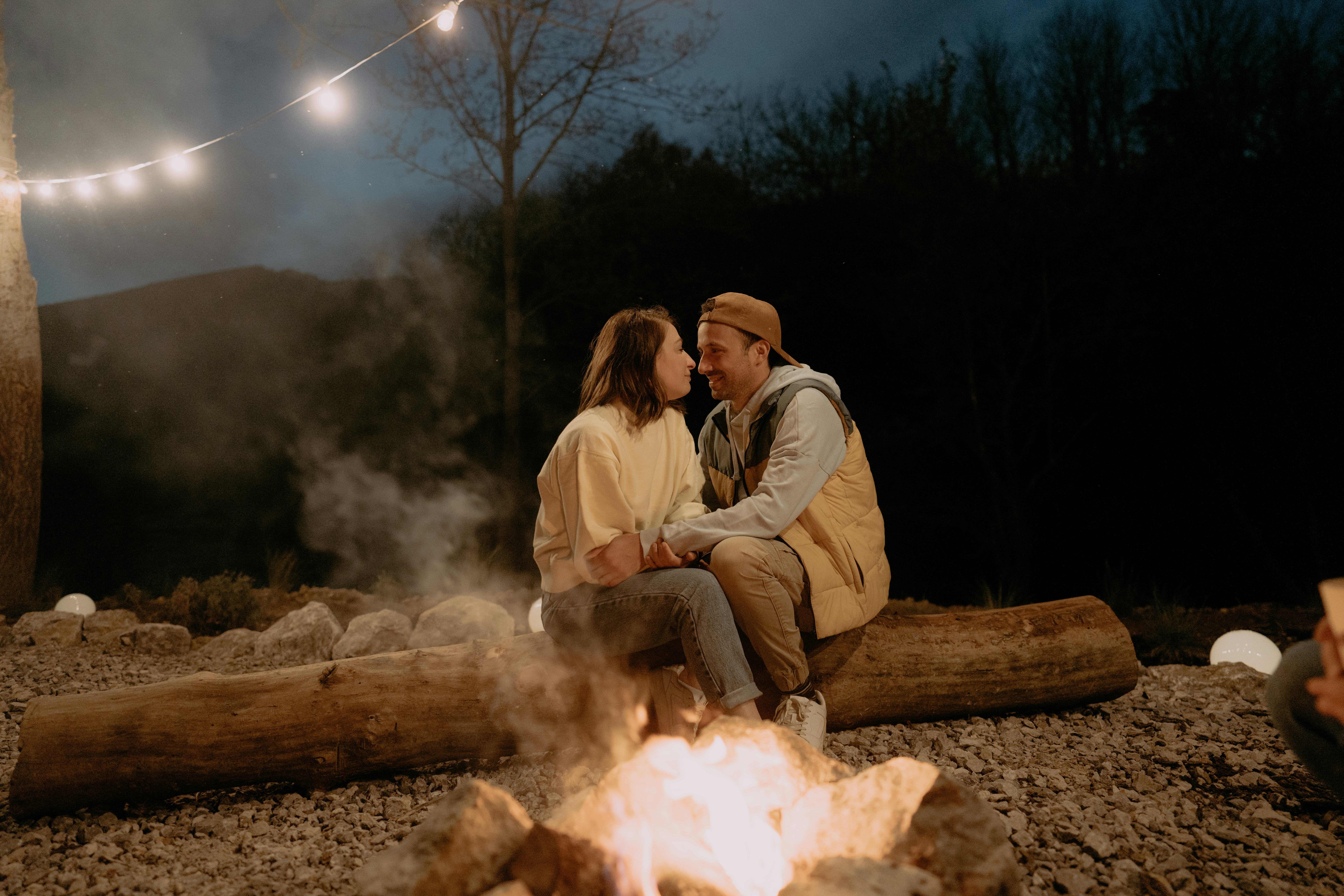 A woman gives her boyfriend some outdoorsy nicknames as they cuddle on a log by a campfire.