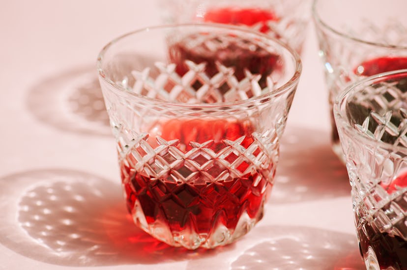 Red wine in a transparent glass with abstract shadows on pink background.