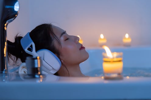 Asian woman luxuriates in the bathtub and closes her eyes, utterly immersed in the soothing melodies…