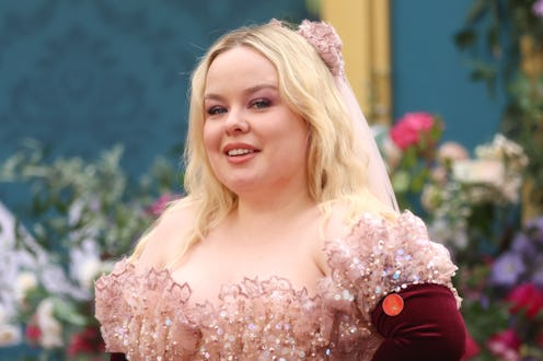 A woman in a glittery pink dress with puffed sleeves and floral accents smiles at a colorful event. ...