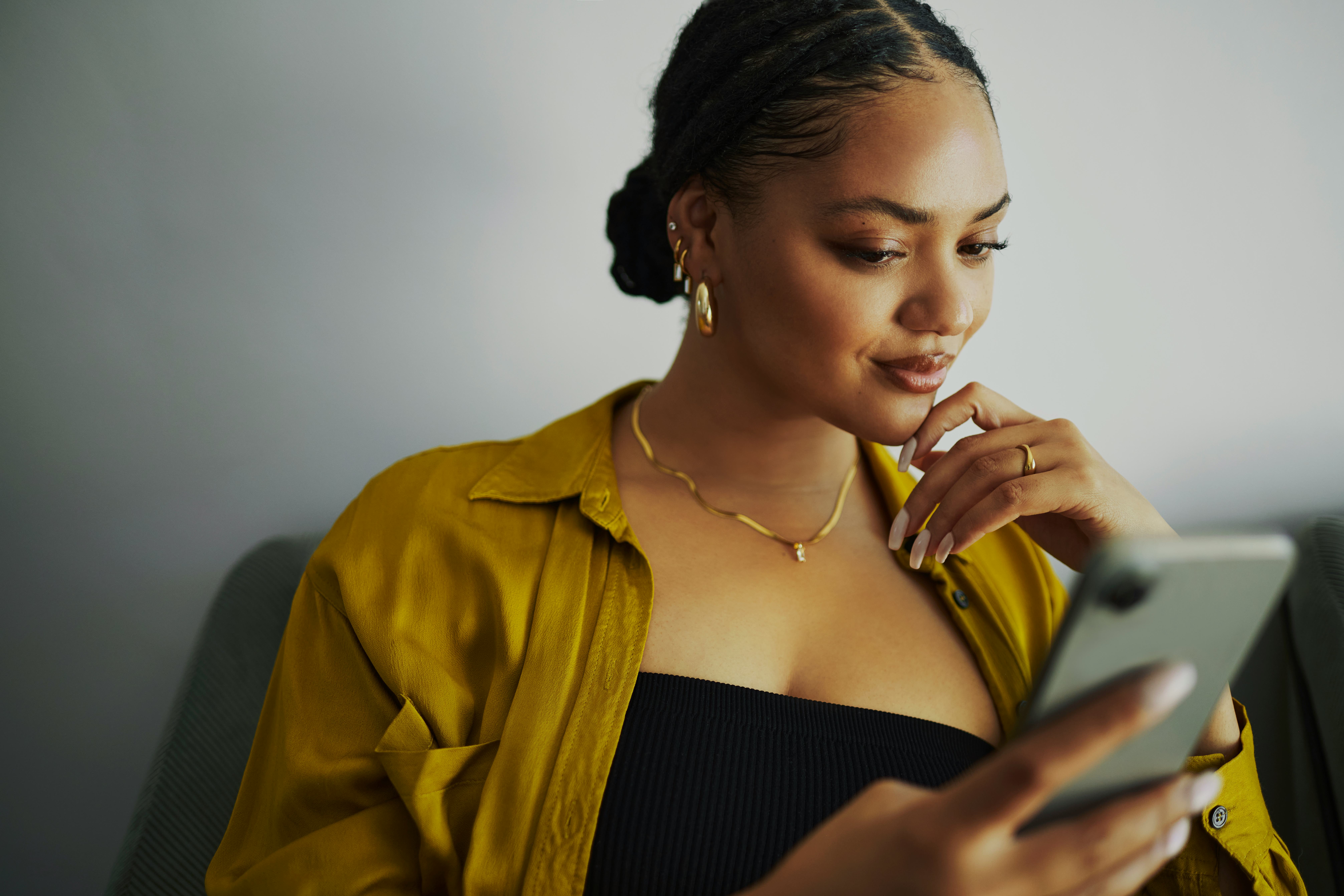 A woman focusing on riddles for adults on her phone and thinking of the answers while on her couch.