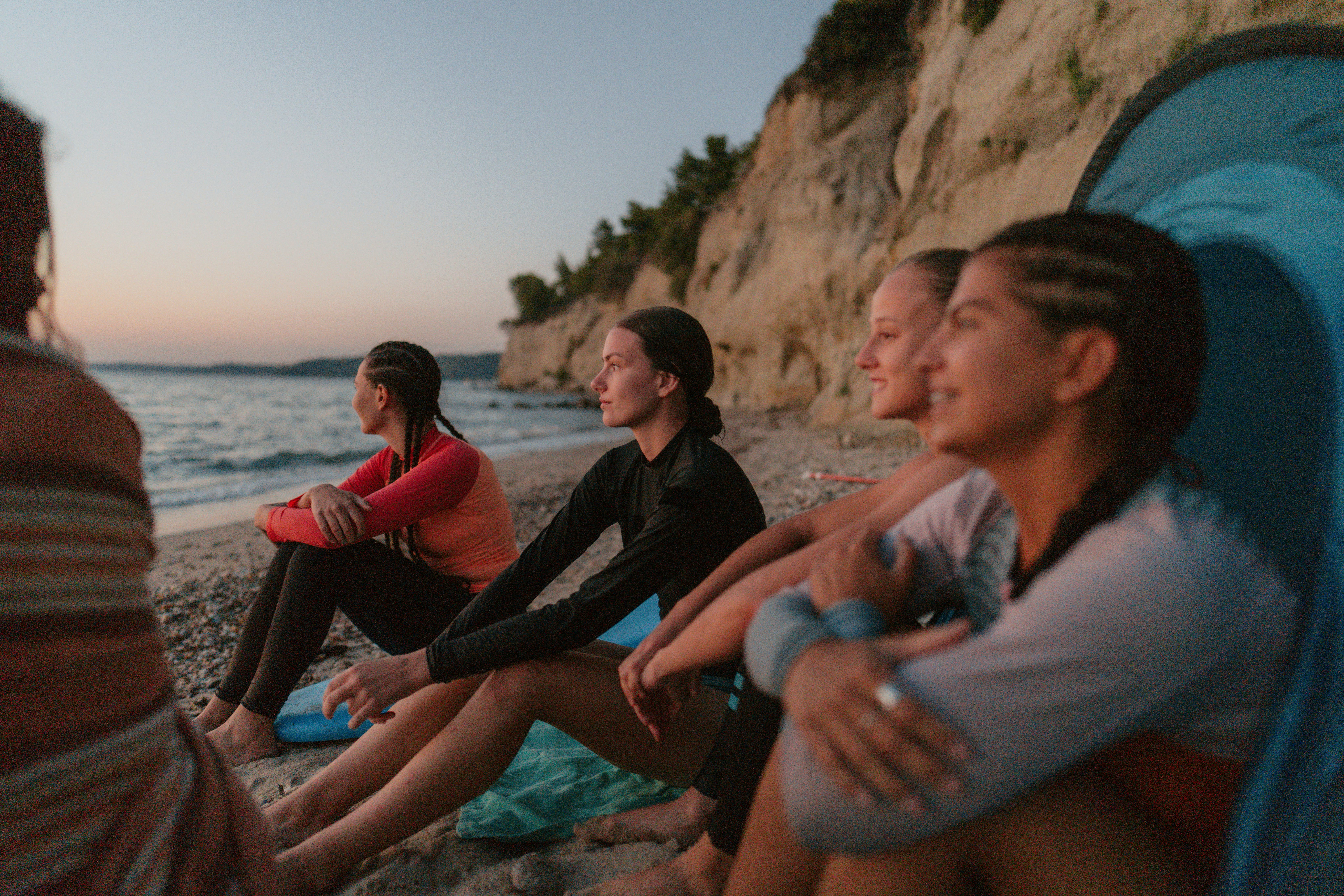 A group of friends sitting at the beach telling each other riddles for adults while looking out at t&hellip;