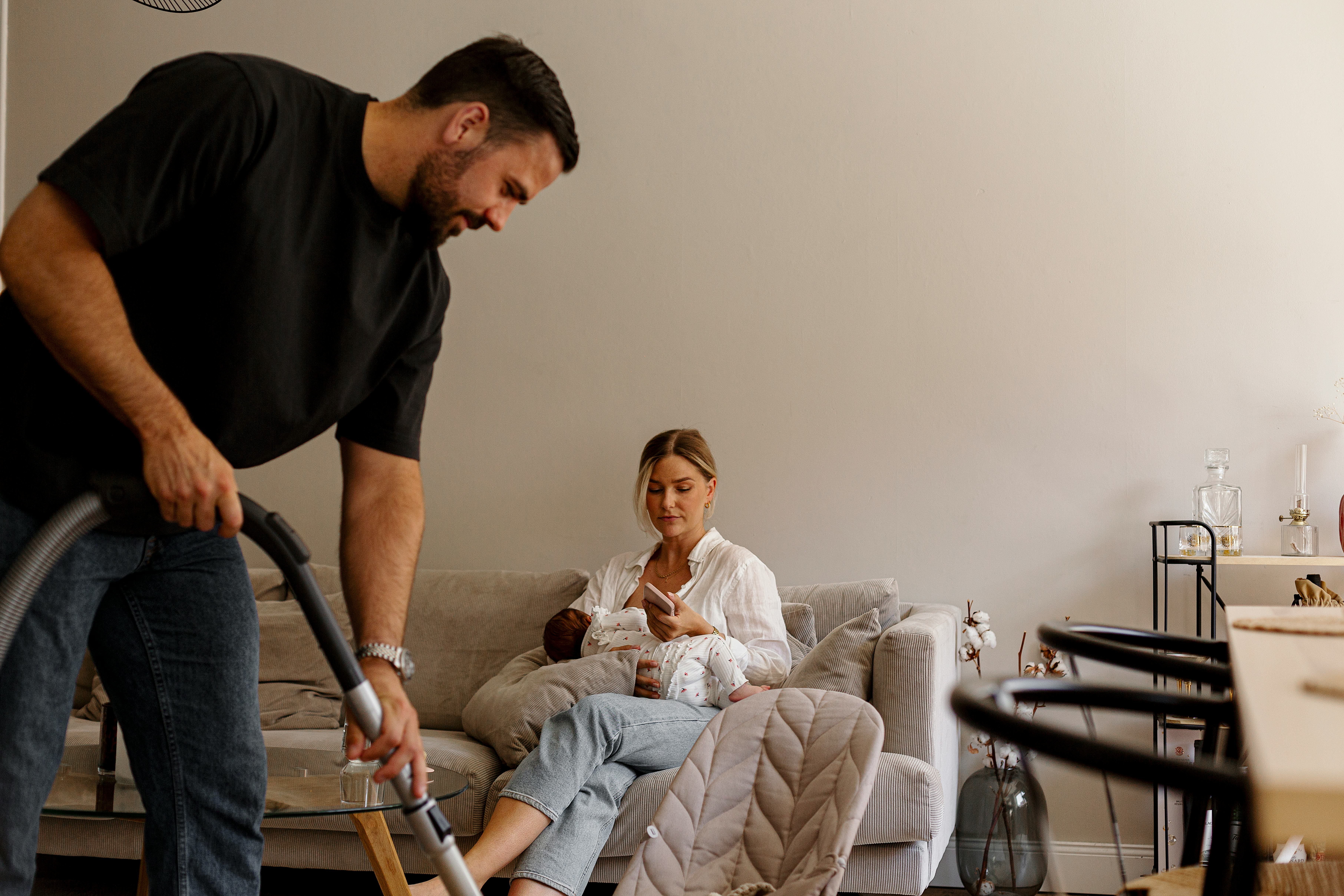 Woman holding baby looking at riddles for adults about the home on her phone in the living room whil&hellip;