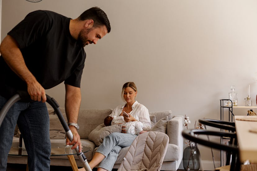 Woman holding baby looking at riddles for adults about the home on her phone in the living room whil…