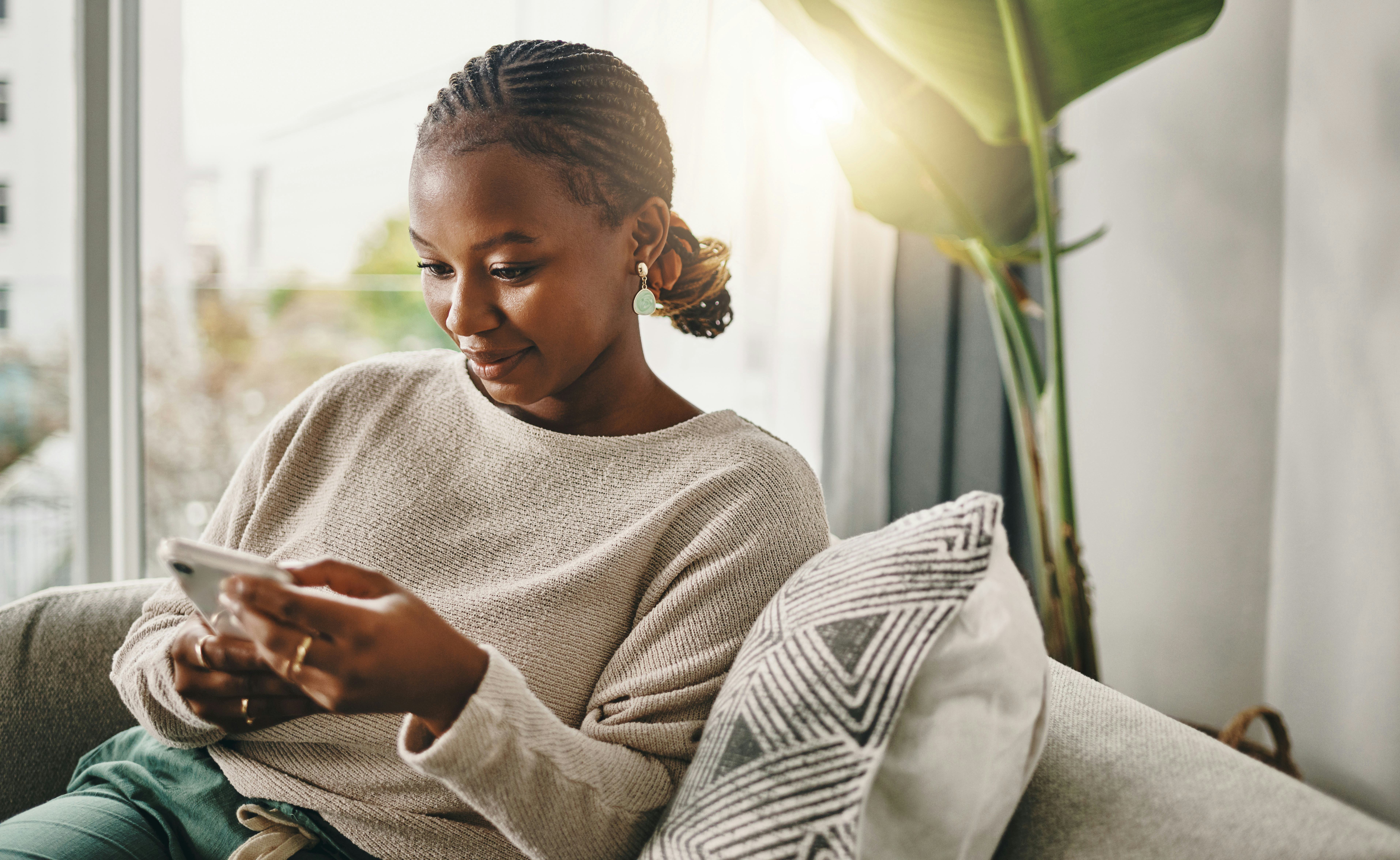 A smart young woman figures out clever adult riddles from her phone while sitting on her couch.