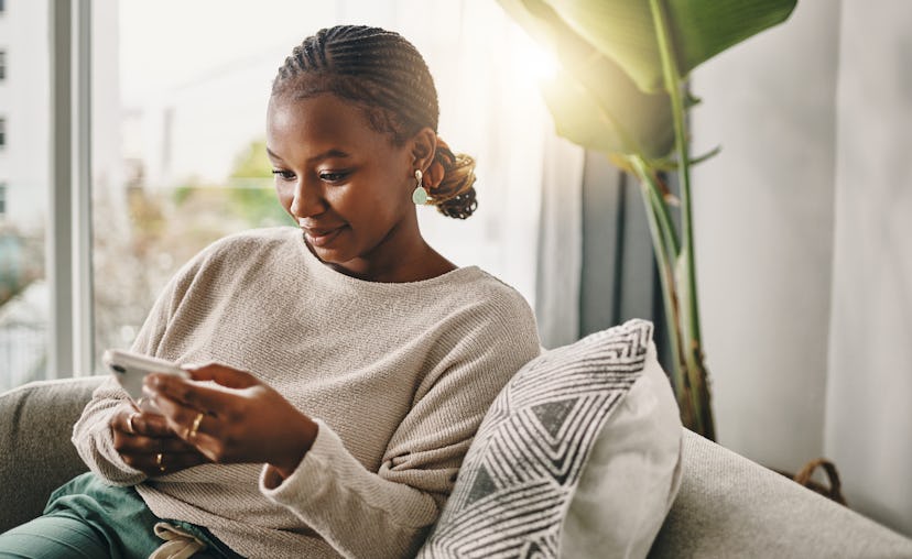 A smart young woman figures out clever adult riddles from her phone while sitting on her couch.