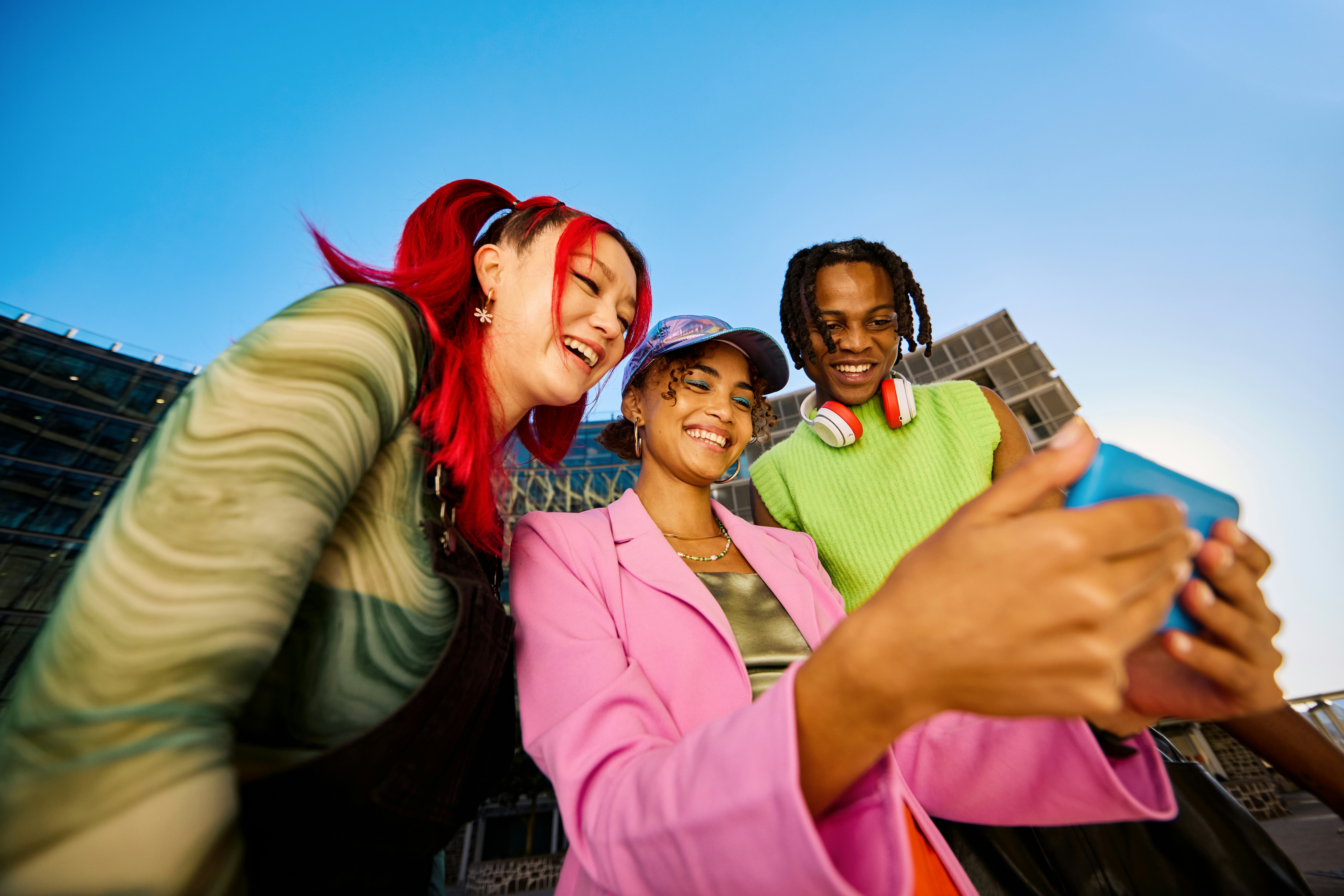A group of three friends smile and try to figure out some brain teaser riddles from their phone.