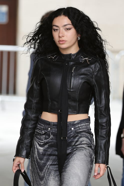Woman with long curly black hair wearing a cropped leather jacket and metallic jeans, walking confid...