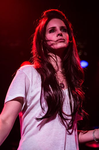 Woman onstage in a white t-shirt, with expressive eyes, and hair windswept across her face under red...