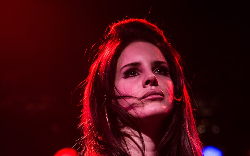 Woman onstage in a white t-shirt, with expressive eyes, and hair windswept across her face under red...