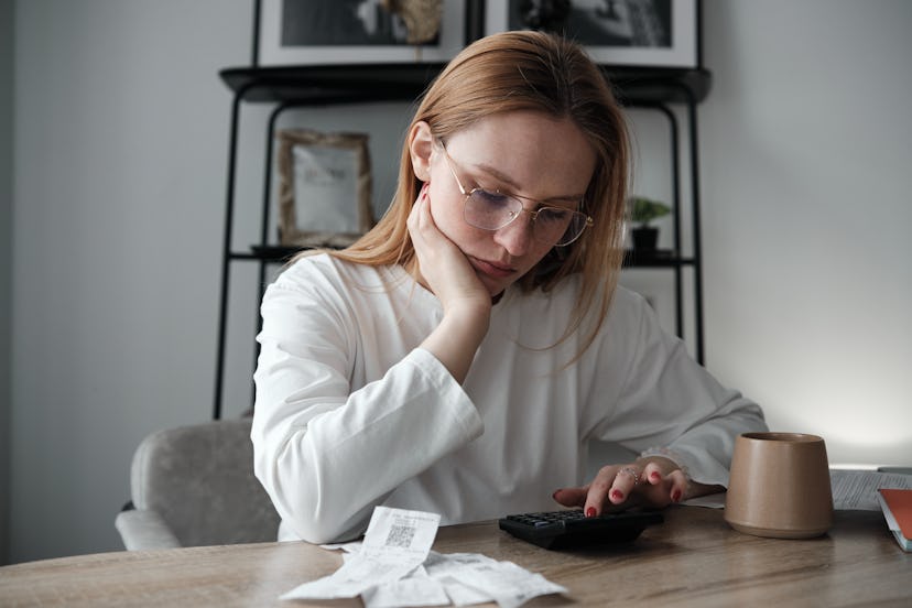 A young woman sits at her dining table with a calculator to try to figure out hard numbers riddles.