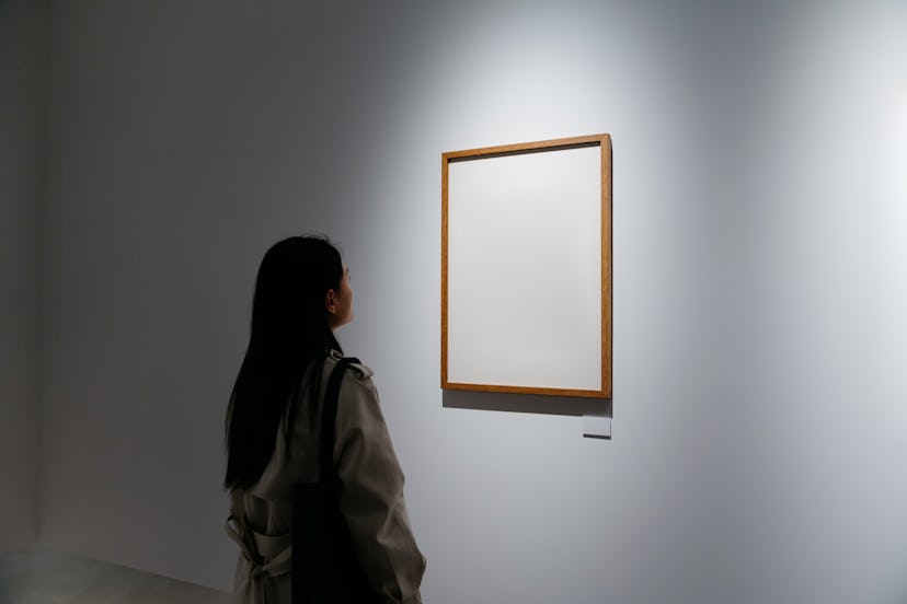 A woman in an art gallery looking at a canvas and contemplating the hard riddles of its history.