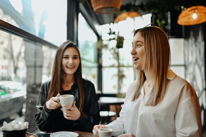 Two female friends are getting coffee at a coffee shop and asking each other hard riddles at their t…