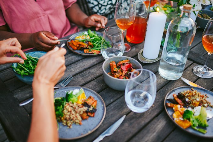 Close-up of a diverse group of women eating a healthy vegan food meal during a dinner party around a...