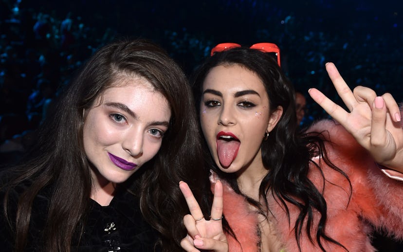 Two young women at an event, one in a black outfit with purple lipstick, the other in green with a r...