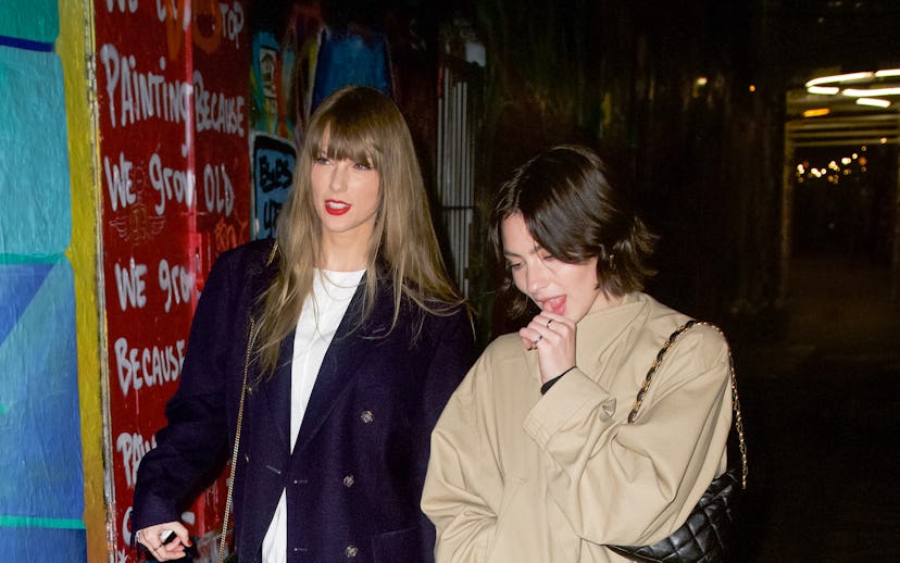 Two women walking in a colorful alley, one dressed in a navy coat and white dress, the other in a be...