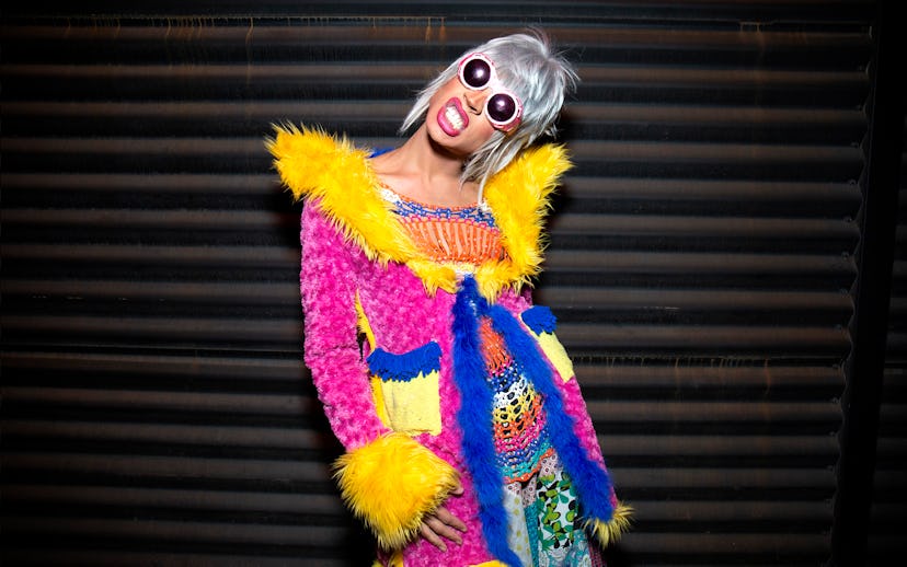 Woman in colorful outfit and sunglasses laughing against a striped background.