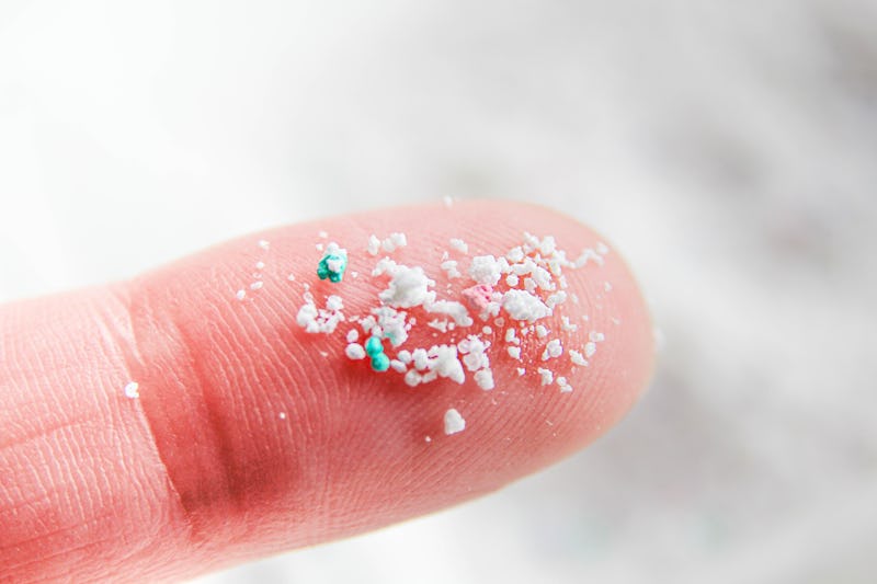 Close-up of a fingertip with white and green microplastic particles scattered on it, against a snowy...