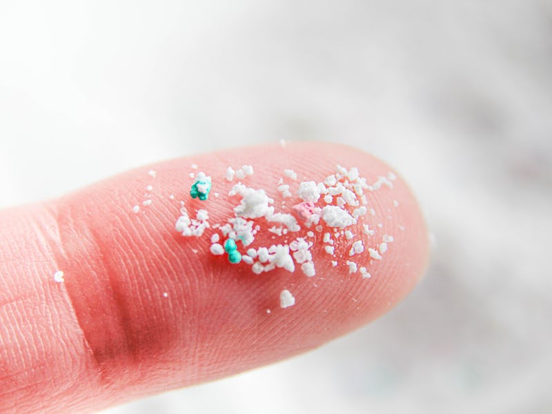 Close-up of a fingertip with white and green microplastic particles scattered on it, against a snowy...