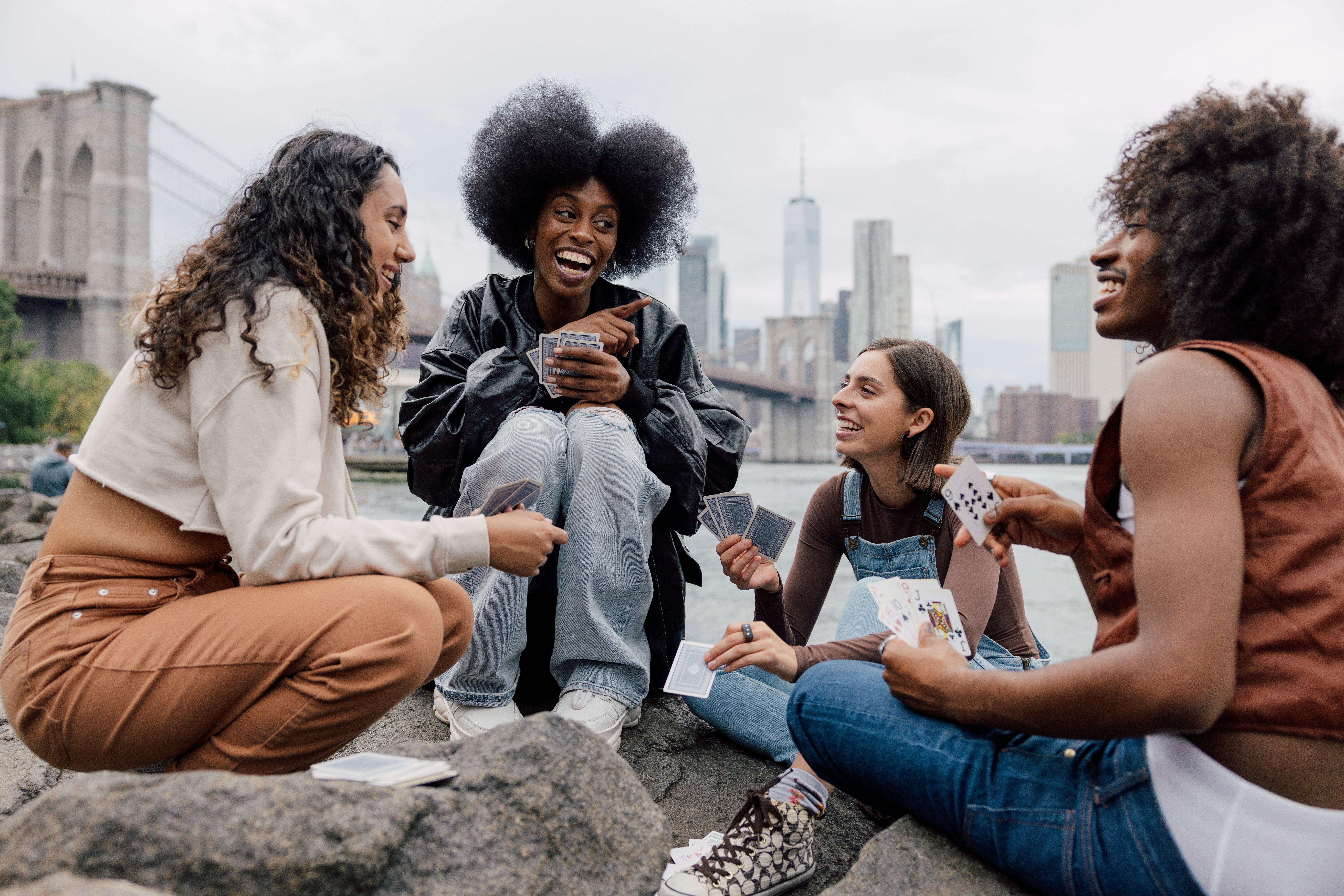 A group of four friends sitting down in front of the New York skyline playing cards and telling fun &hellip;