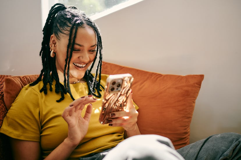 A young woman sitting on her couch and learning fun facts on her phone.