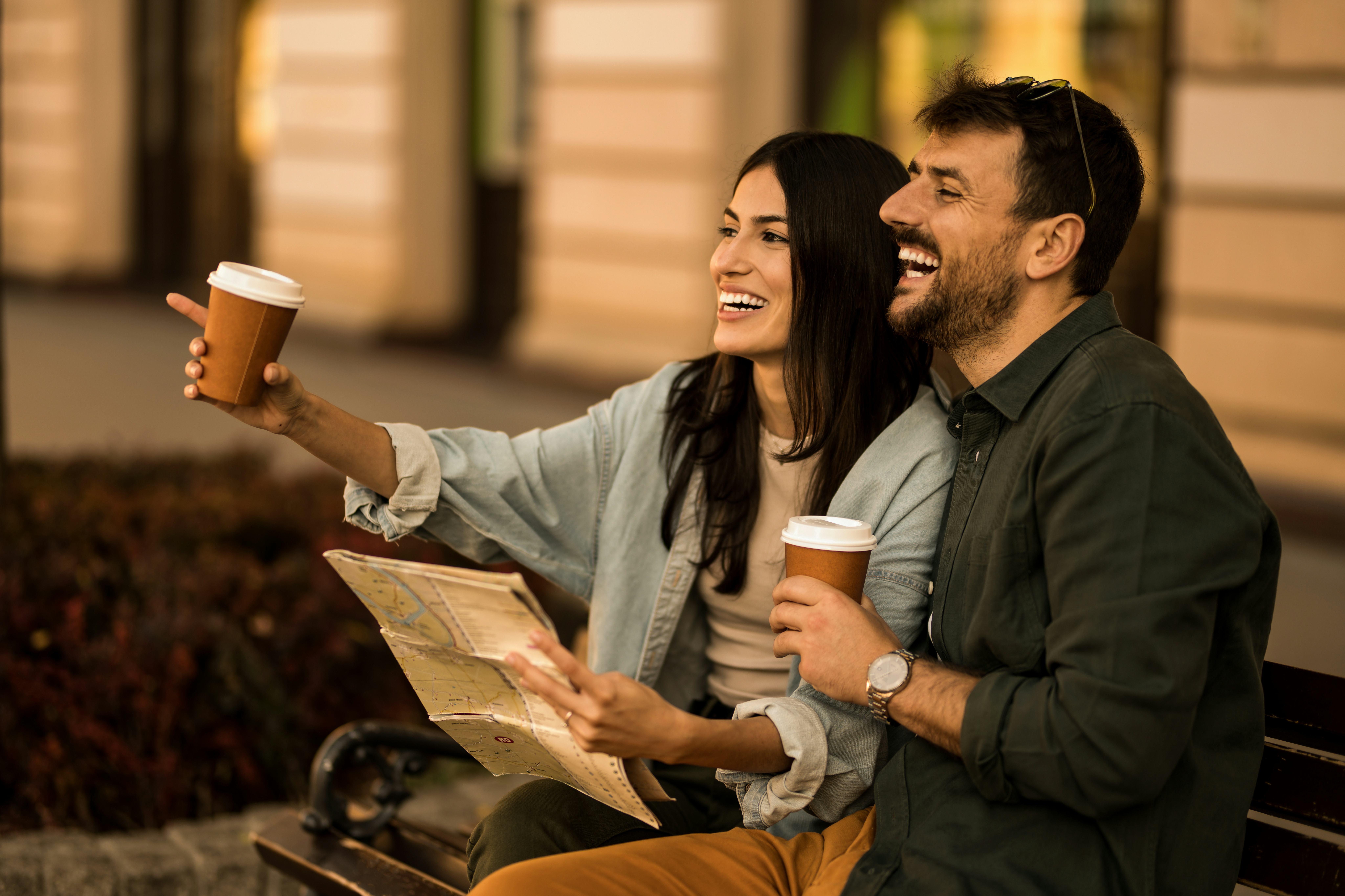 A couple smiling sitting on a bench and and learning geography facts looking at a map.