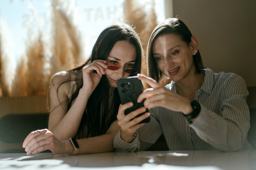 Two friends looking at random facts on a phone as the sit at a coffe shop table.