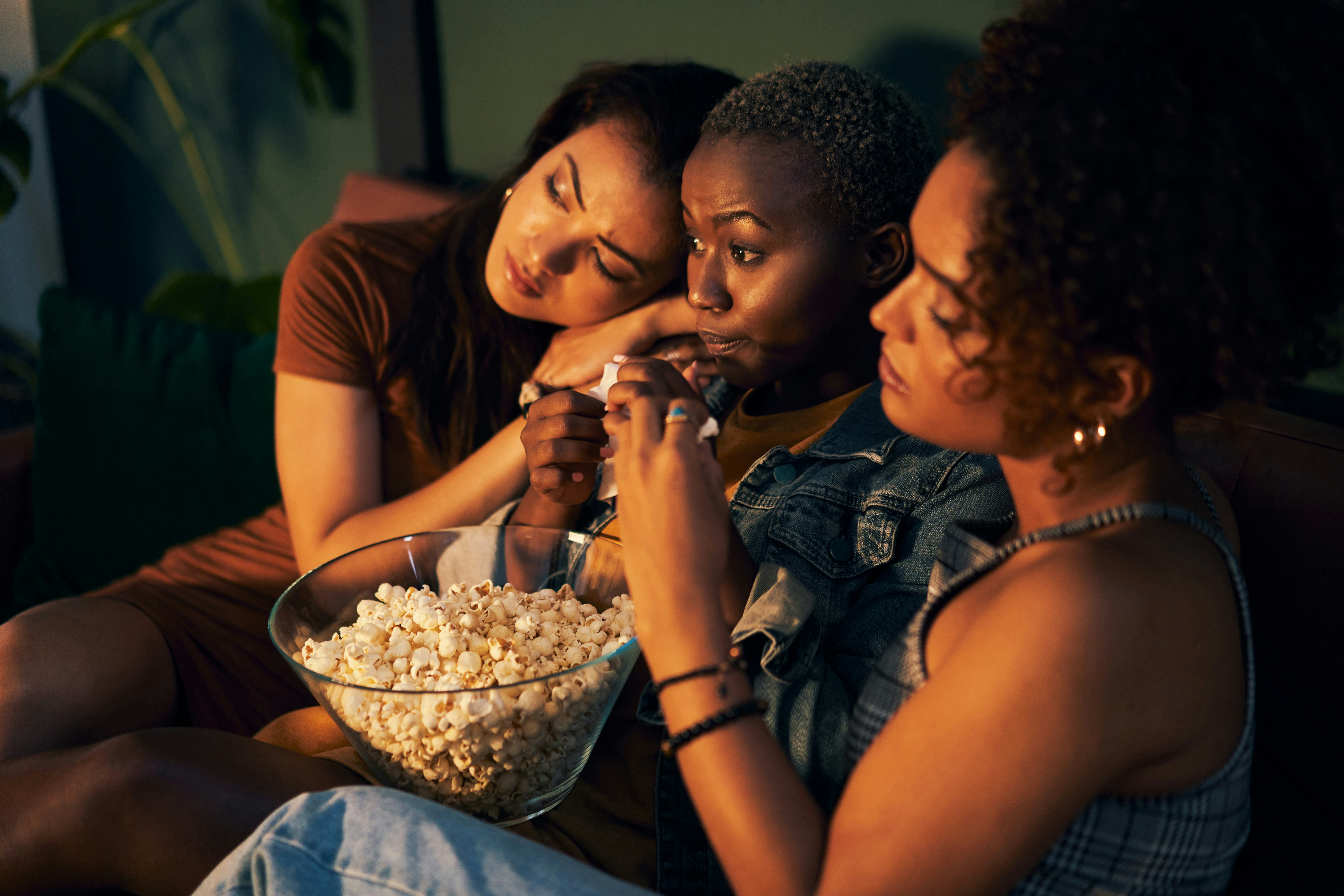 Three friends sitting on a couch and eating popcorn while watching a movie and learning new facts.