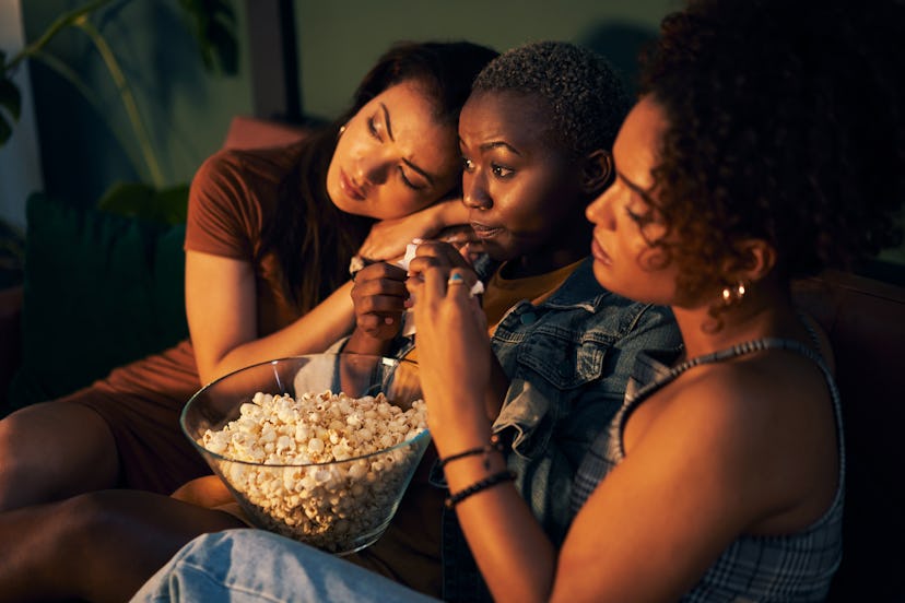 Three friends sitting on a couch and eating popcorn while watching a movie and learning new facts.