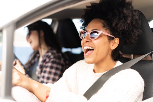 View from outside the car window of three happy female friends singing during road trip