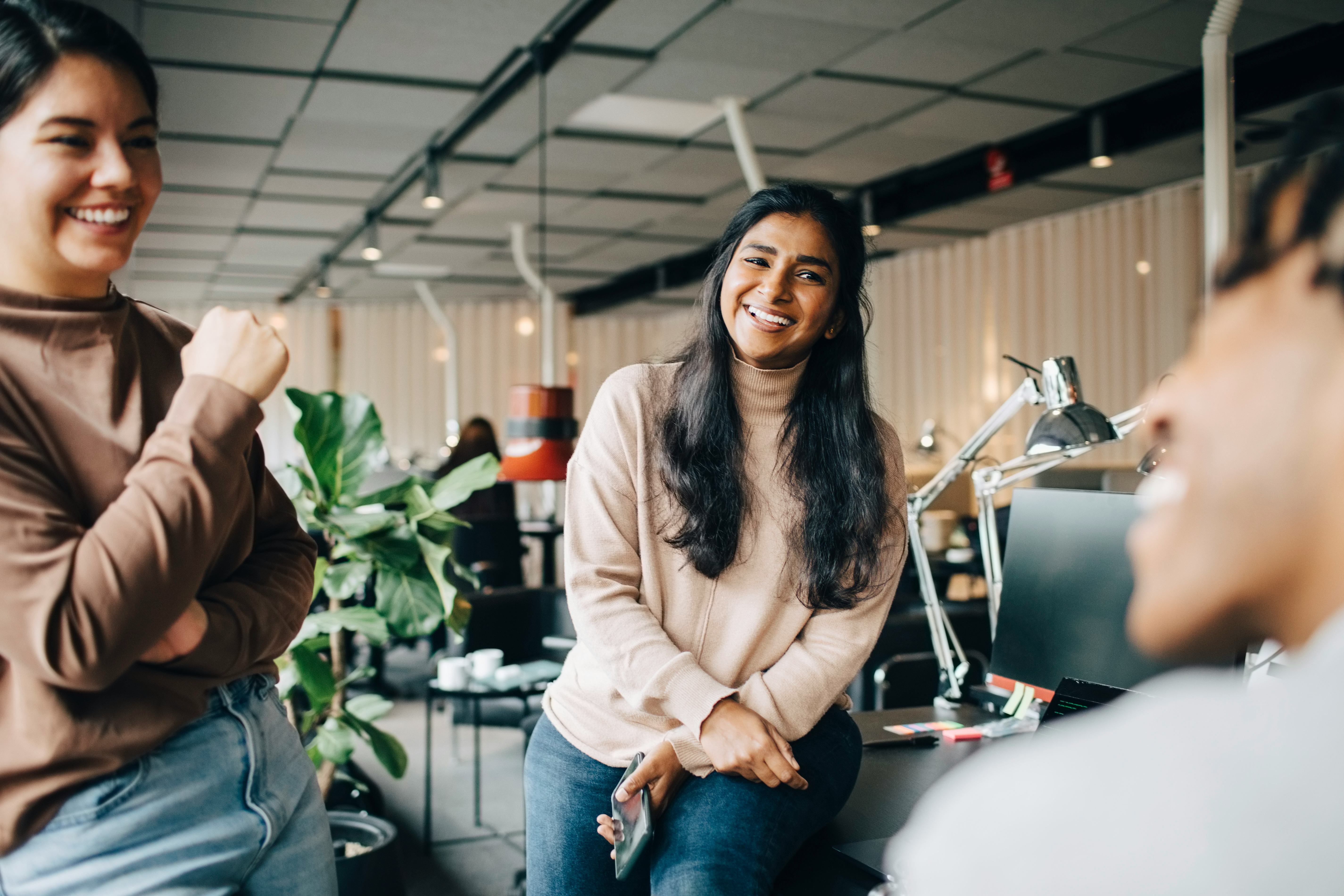 Three colleagues swap fun facts about themselves and laugh in the office.