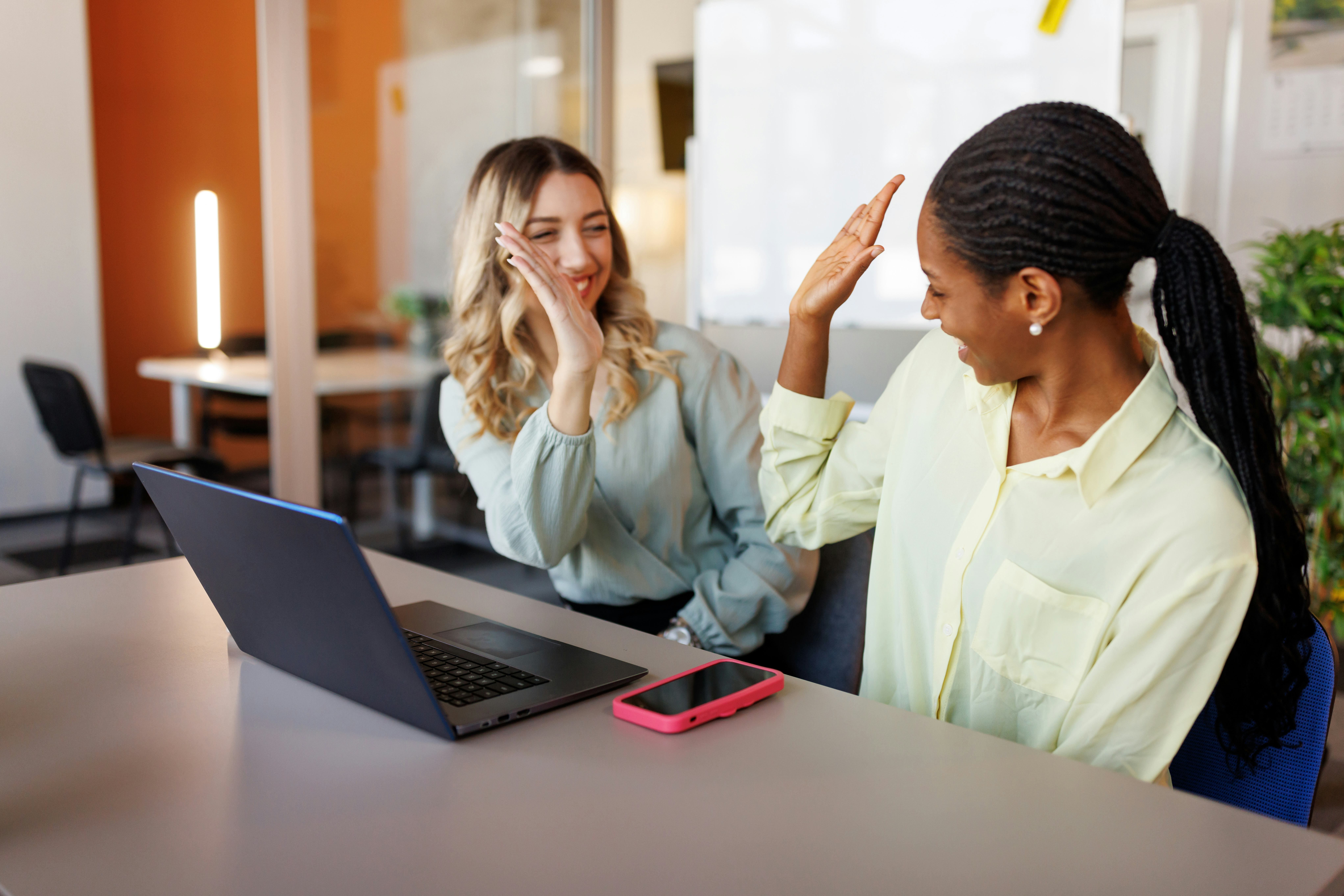 Two young women colleagues high five over their fun facts about me answers at work.