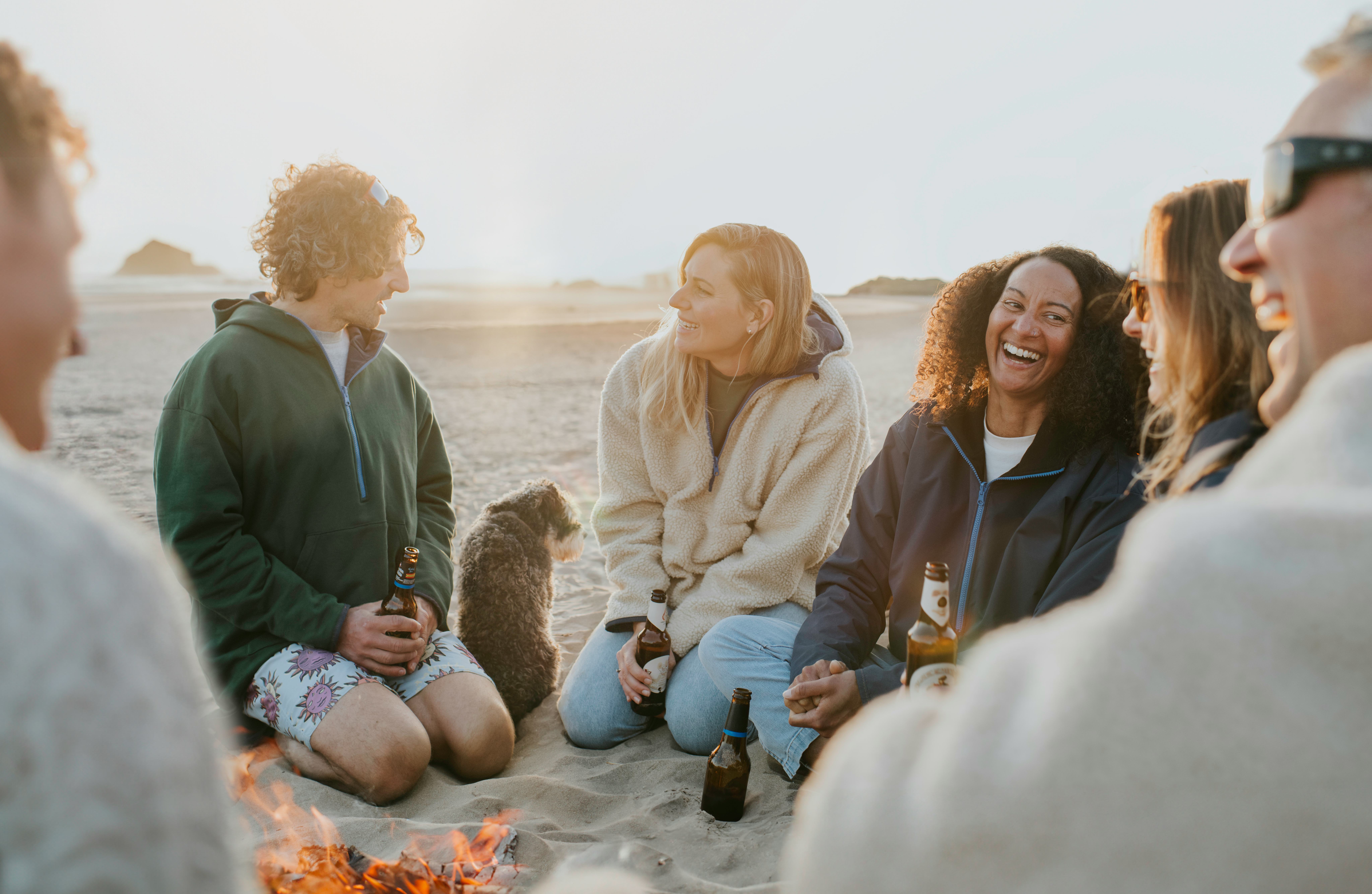 Friends sharing fun facts about themselves in a circle around a campfire on the beach.