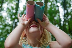 Four year old girl looking up through home made toy binocolors in forest