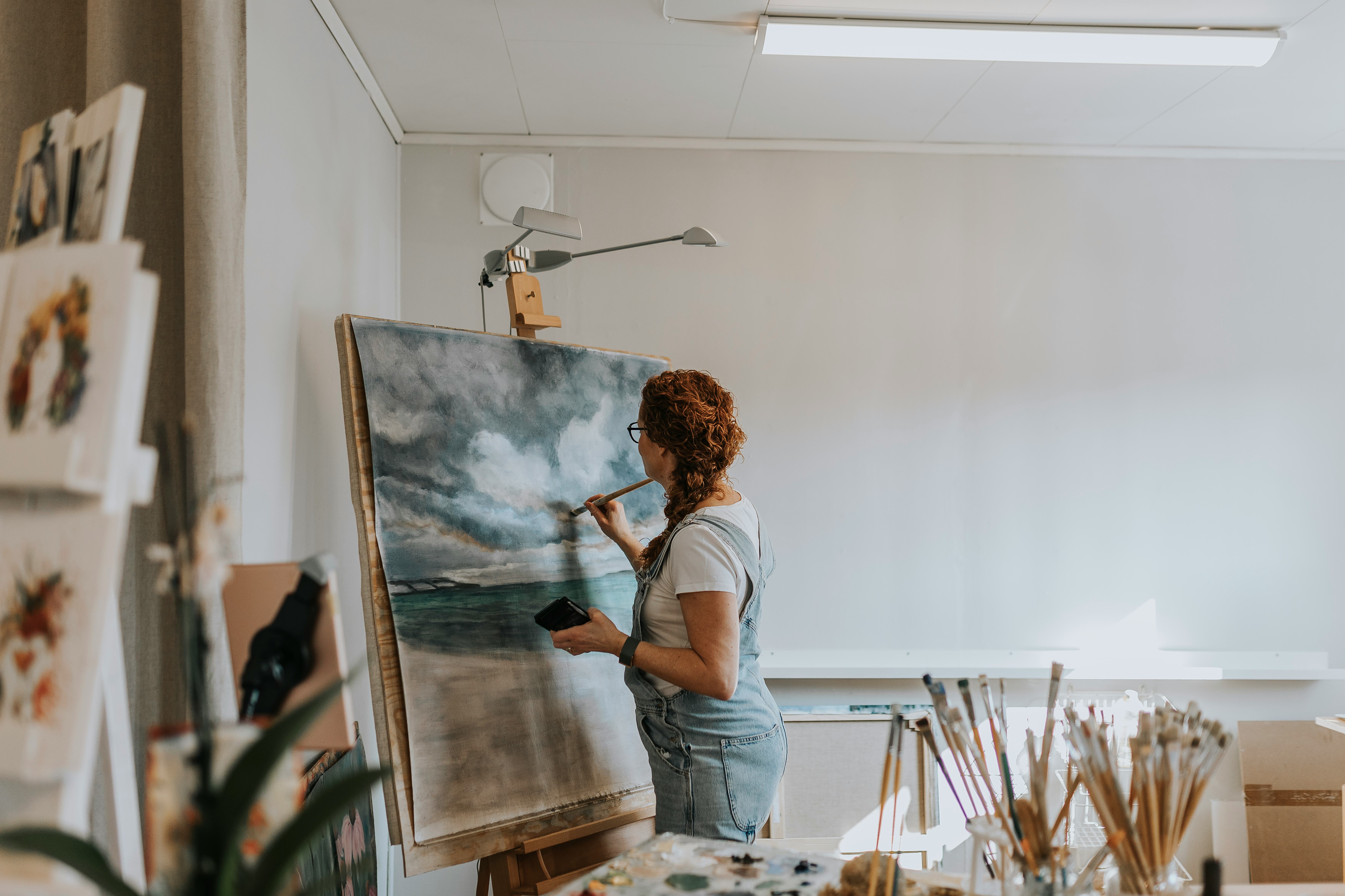 A woman artist painting an ocean scene on a canvas in her home studio.