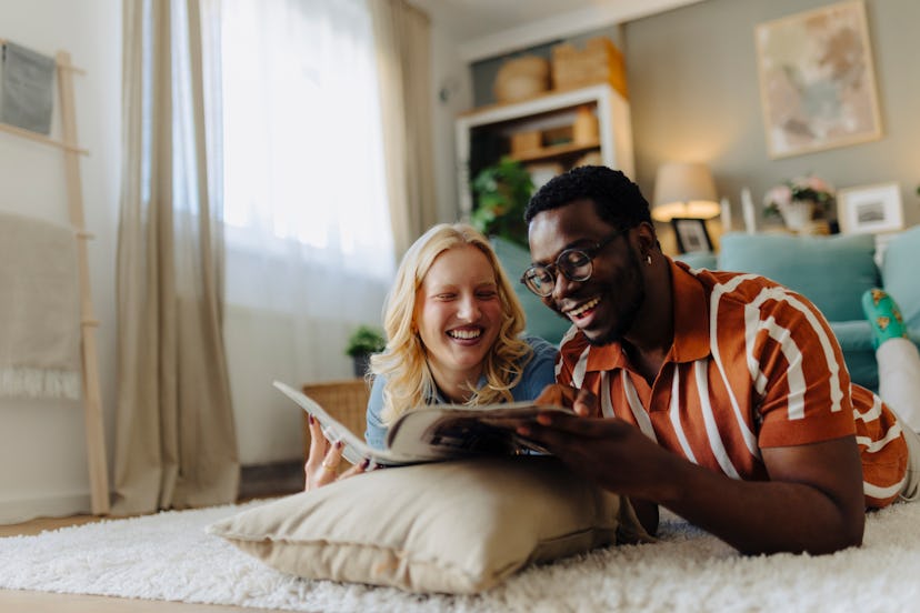 A young couple laying on the floor and reading a book on fun facts about me ideas and smiling.