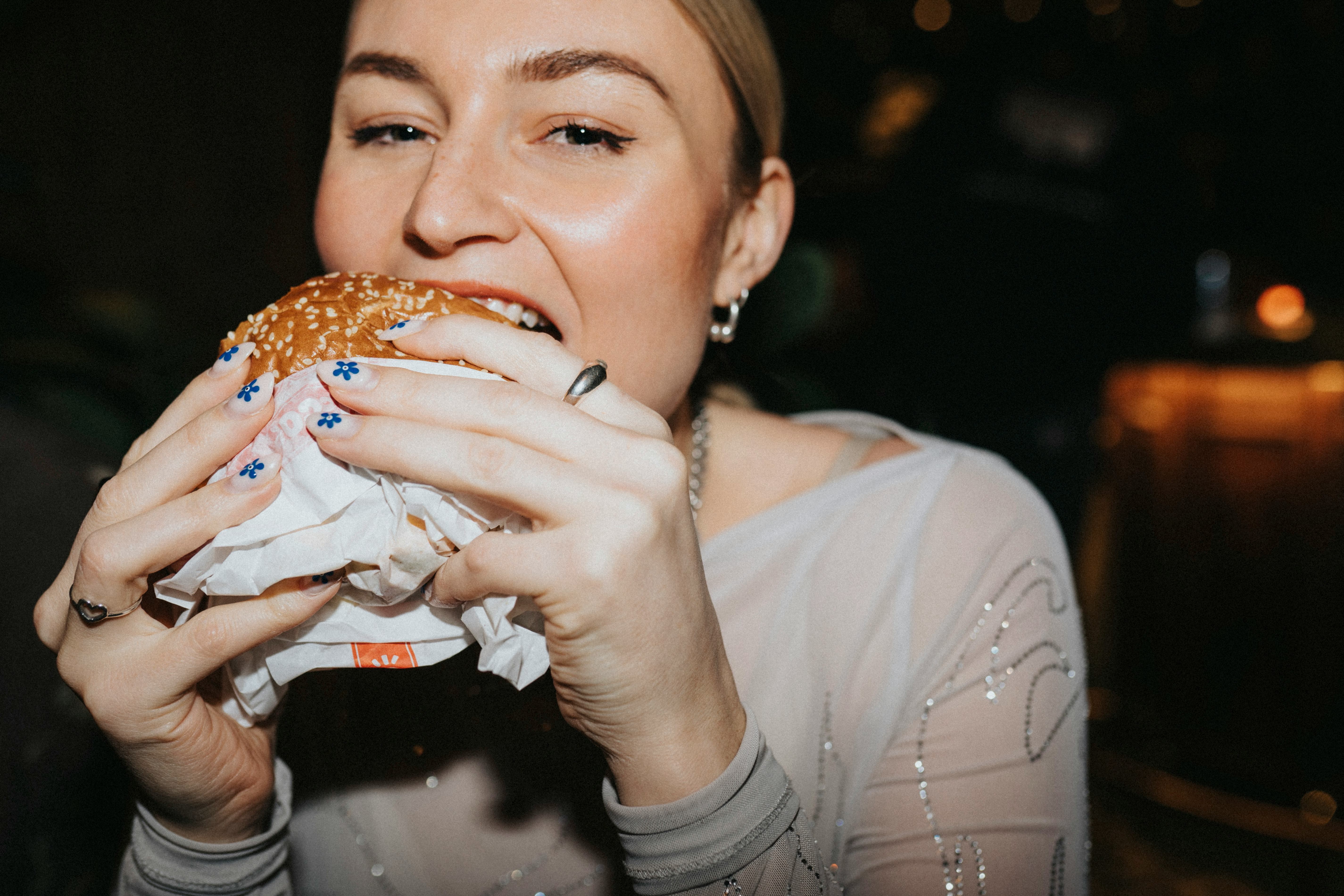 A close up flash photo of a young woman taking a bite out of a hamburger.