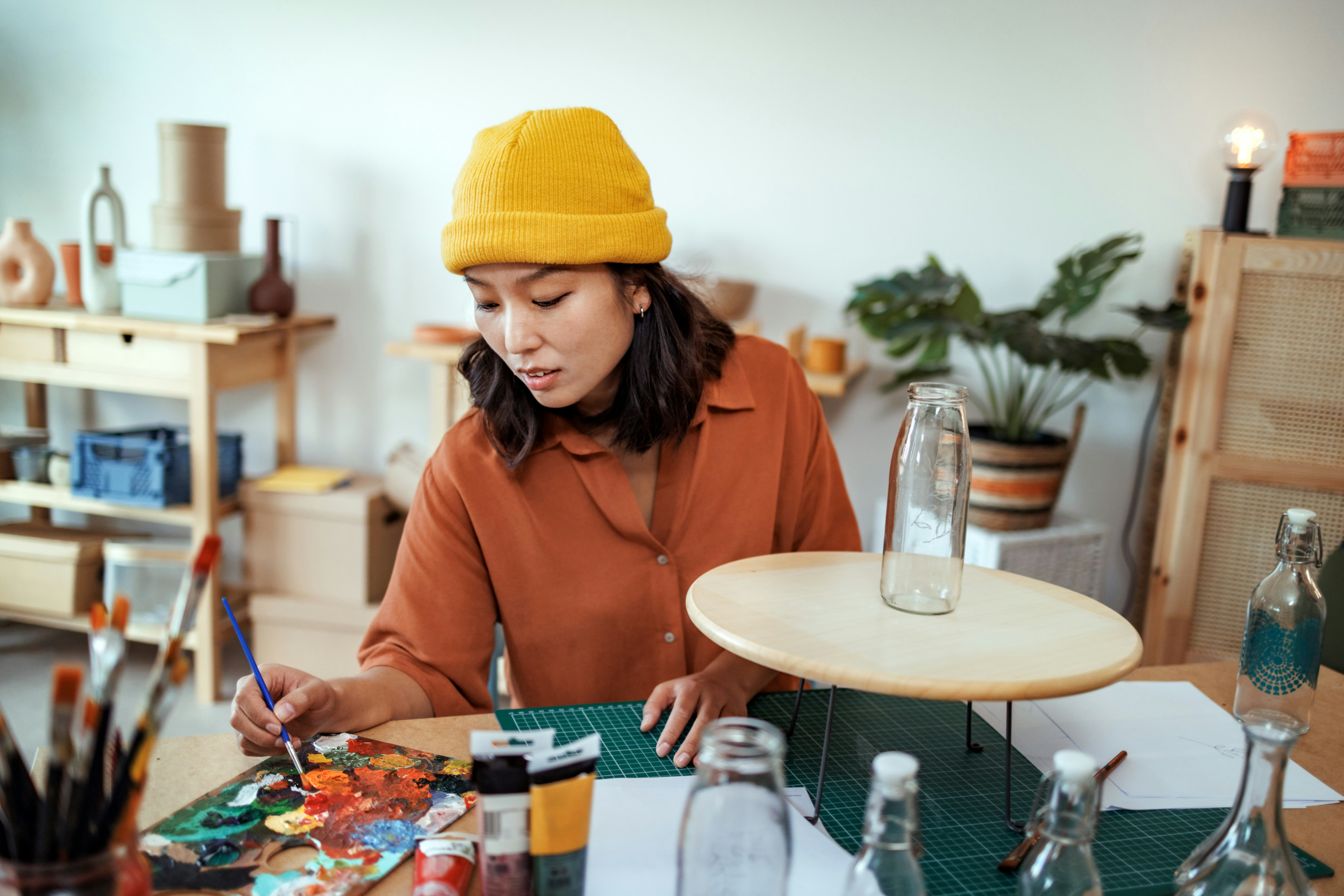 A young woman painting glass bottles in her art studio.