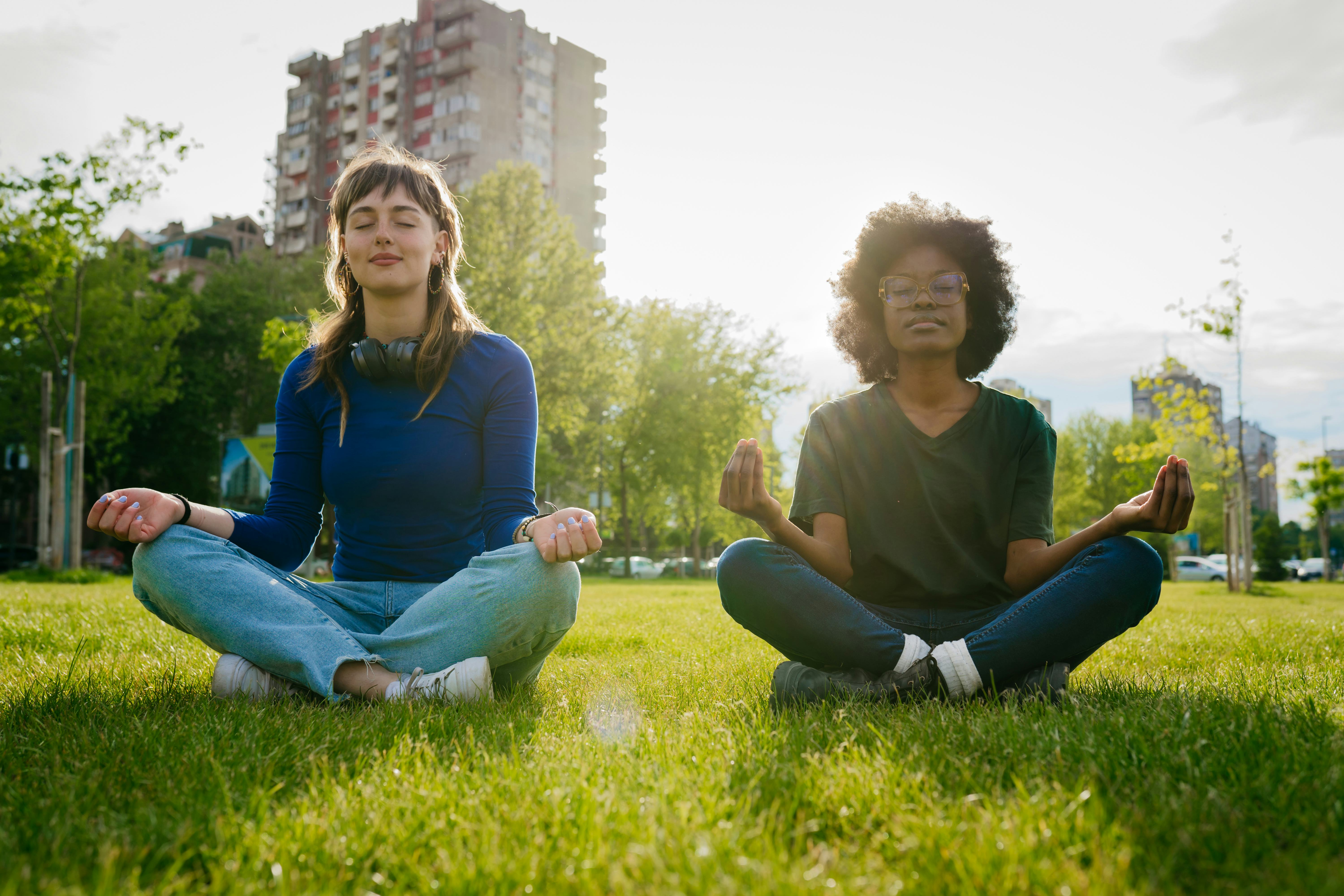 Two young woman meditate in the park and share fun facts about me with each other.