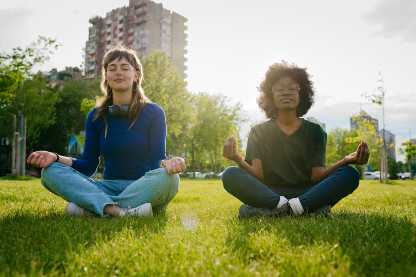 Two young woman meditate in the park and share fun facts about me with each other.