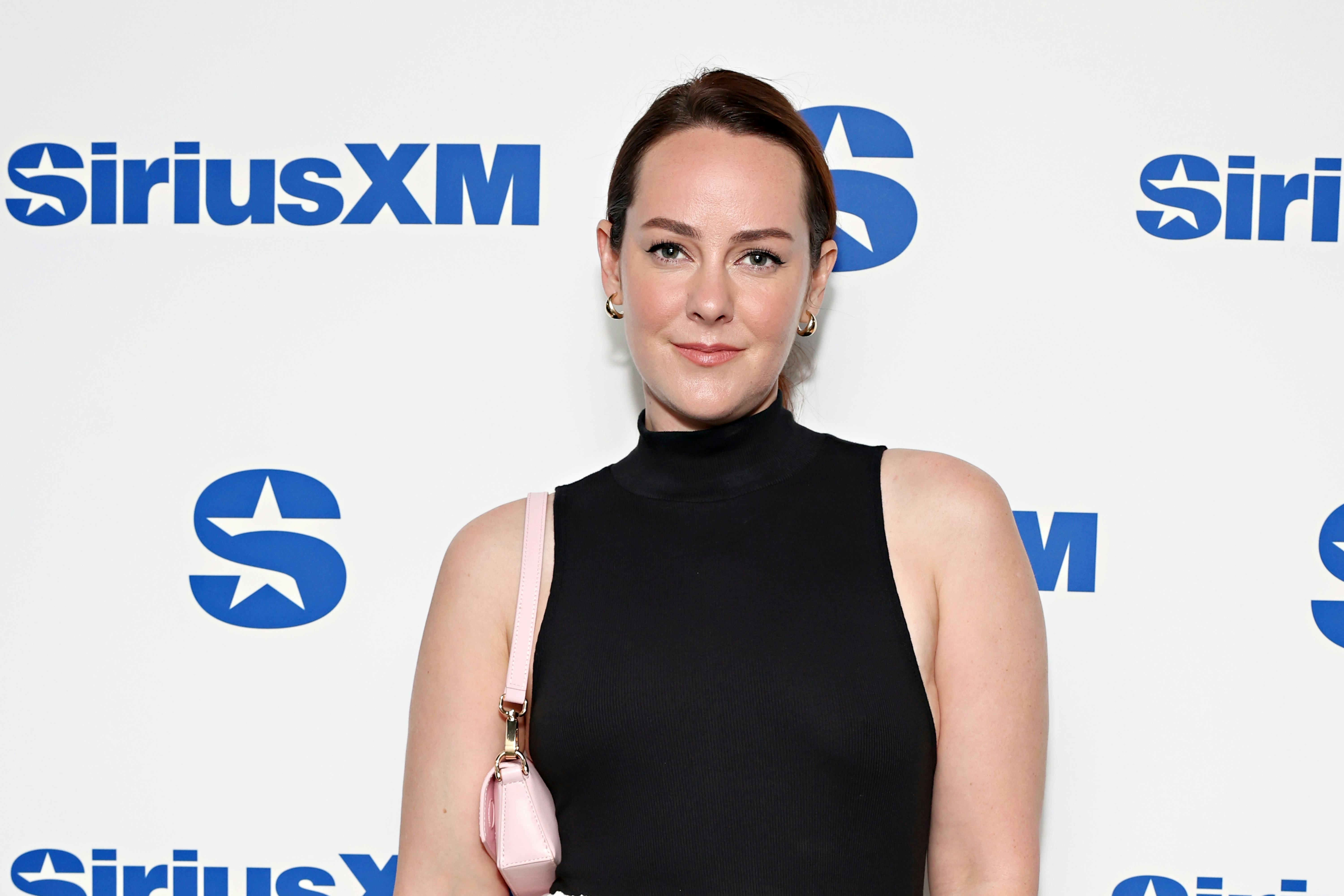 Woman in black turtleneck and pink purse posing in front of a SiriusXM backdrop.