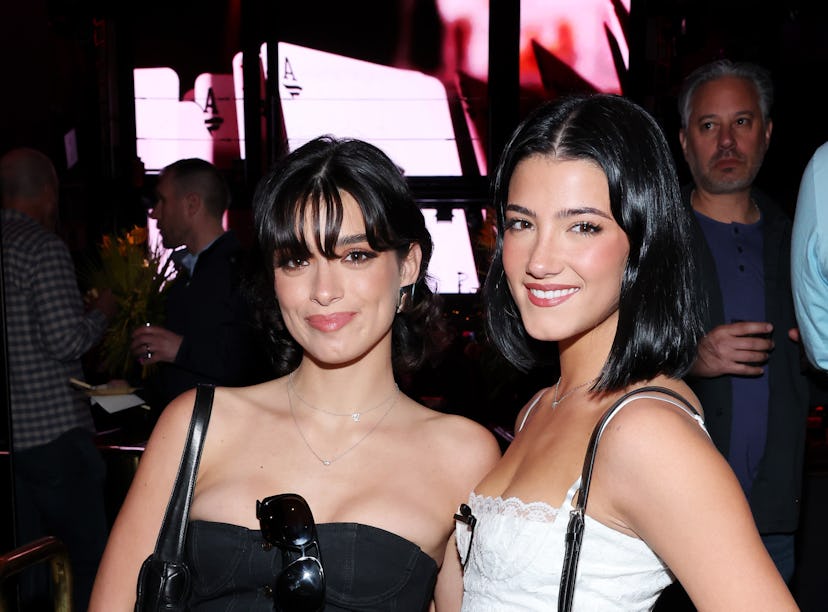 Two women smiling in a club, one in a black dress and the other in white, both wearing small purses.