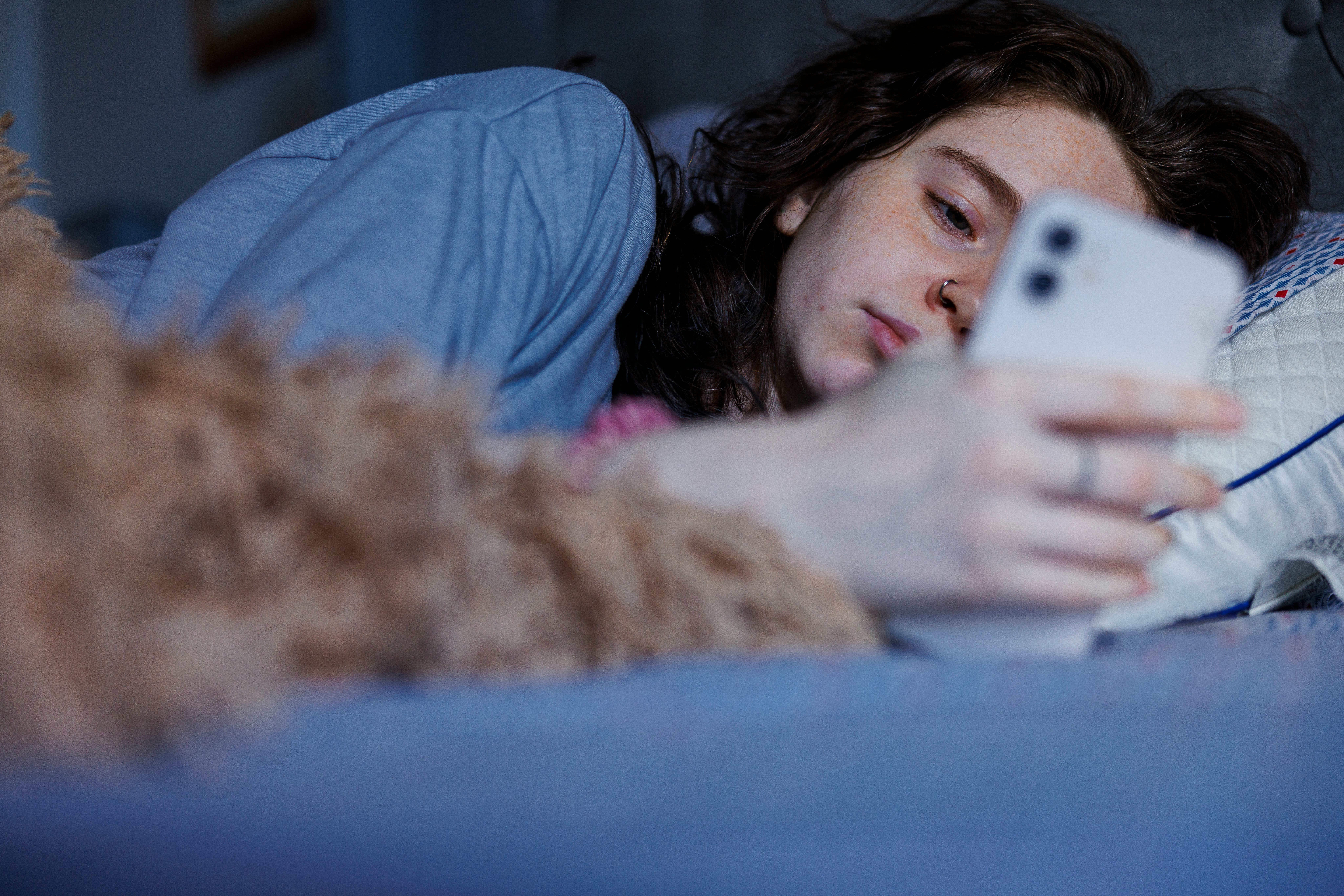An Exhausted Caucasian brunette woman wakes up with a smartphone in hand after a restless night in bed.