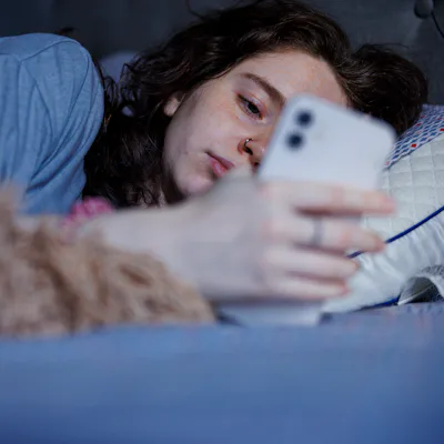 An Exhausted Caucasian brunette woman wakes up with a smartphone in hand after a restless night in bed.